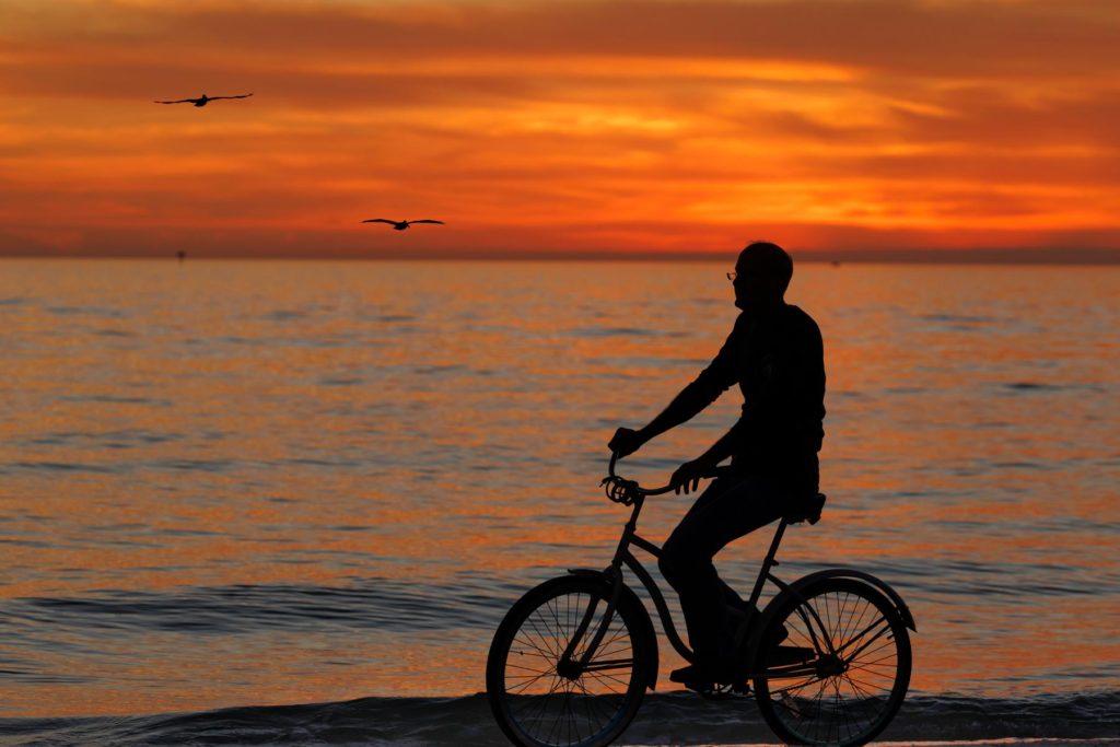 man riding bicycle on beach at sunset