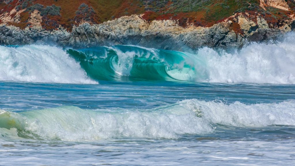 Breaking wave against the rocky cliffs at Garapatos State Beach in California