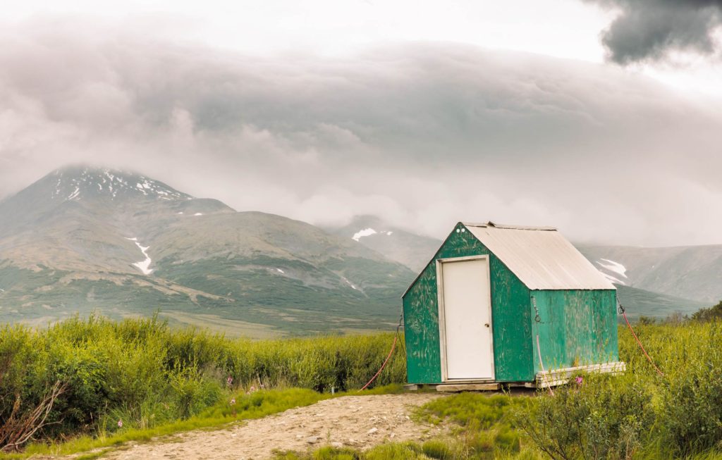 green outhouse building against Alaska mountain and stormy sky at Pilgrims hot springs
